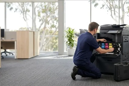 A technician kneeling at an open copier with the colour toner units exposed